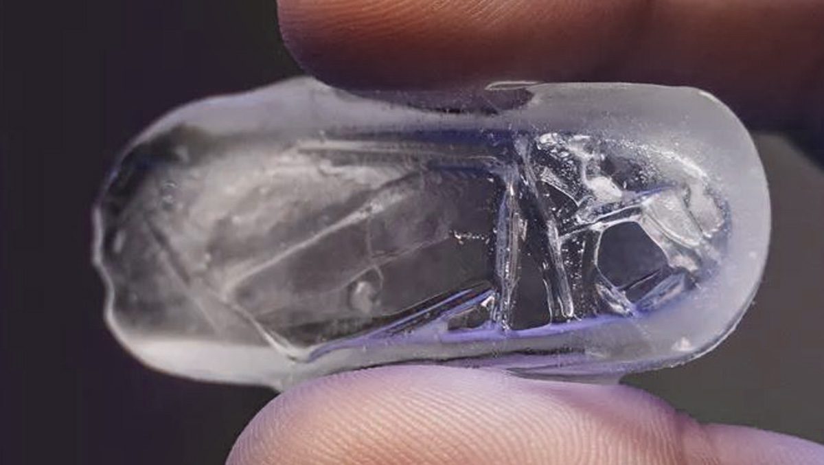 Close-up view of a person holding a thin and hollow ice cube, indicating potential issues with ice maker functionality.